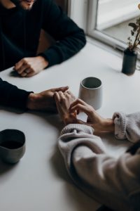 A couple holding hands across a table with a cup of coffee.